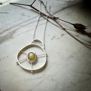 May include: A silver necklace with a circular pendant featuring a yellow gemstone set in a geometric design.
