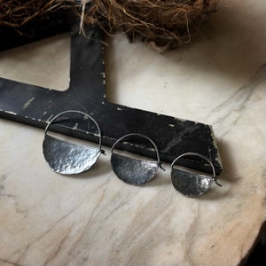 May include: Three silver hoop earrings with a hammered, half-circle design. The earrings are different sizes, with the largest earring on the left and the smallest earring on the right.