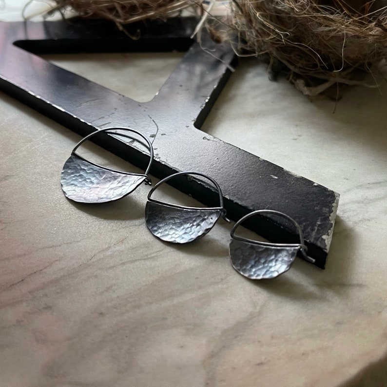 May include: Three silver hoop earrings with a hammered texture. The earrings are in the shape of a half circle.