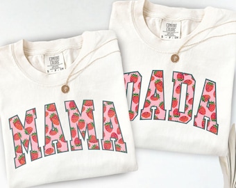 May include: Two cream-colored t-shirts with a strawberry print. One shirt says "MAMA" and the other says "DADA".