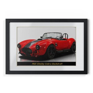 May include: Framed print of a red 1965 Shelby Cobra Backdraft sports car with black racing stripes. The car has black wheels and a roll bar. The text "1965 Shelby Cobra Backdraft" is at the bottom.