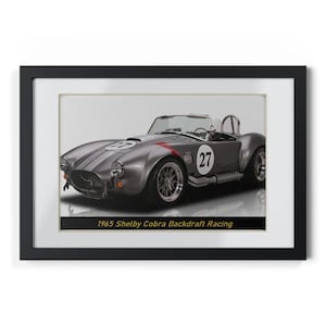 May include: Framed print of a gray 1965 Shelby Cobra Backdraft Racing car. The car has the number 27 on the side and hood. Red accent stripes are visible. The print is in a black frame with a white mat.