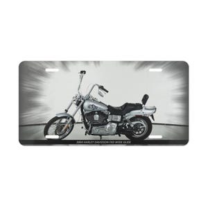 May include: A license plate featuring a silver motorcycle with black accents. The motorcycle has a tall handlebar and a black seat. The text "2004 HARLEY DAVIDSON FXD WIDE GLIDE" is printed at the bottom of the plate.