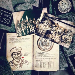 May include: An open notebook with sketches and text, alongside two photographs and patches. The notebook features a drawing of a man in a military uniform and a list of names. The photographs depict soldiers. Patches include a skull and wings design.