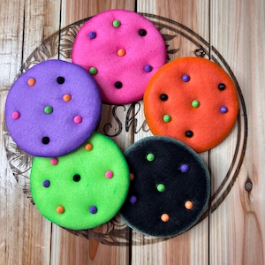 May include: Five felt circles with different colors and patterns. The circles are decorated with black, orange, green, and purple dots. The colors of the circles are pink, purple, green, black, and orange.