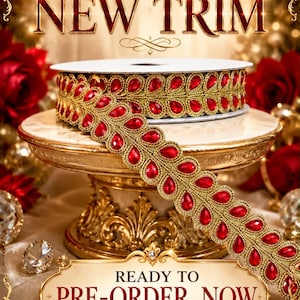 May include: A spool of gold-toned trim featuring a repeating pattern of red teardrop-shaped gems. The text EXCLUSIVE NEW TRIM and READY TO PRE-ORDER NOW is displayed in the image. The trim is coiled on a stand with a metallic gold finish.