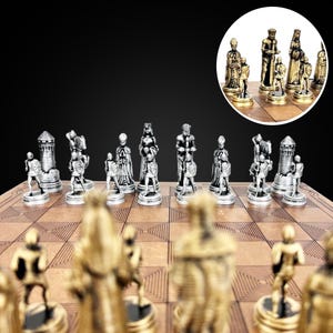 Könnte beinhalten: Ein Schachspiel in Silber und Gold mit Figuren in Form mittelalterlicher Figuren. Das Schachbrett ist aus Holz und hat eine hellbraune Oberfläche.