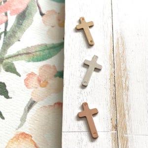 May include: Three metal cross charms in gold, silver, and rose gold.