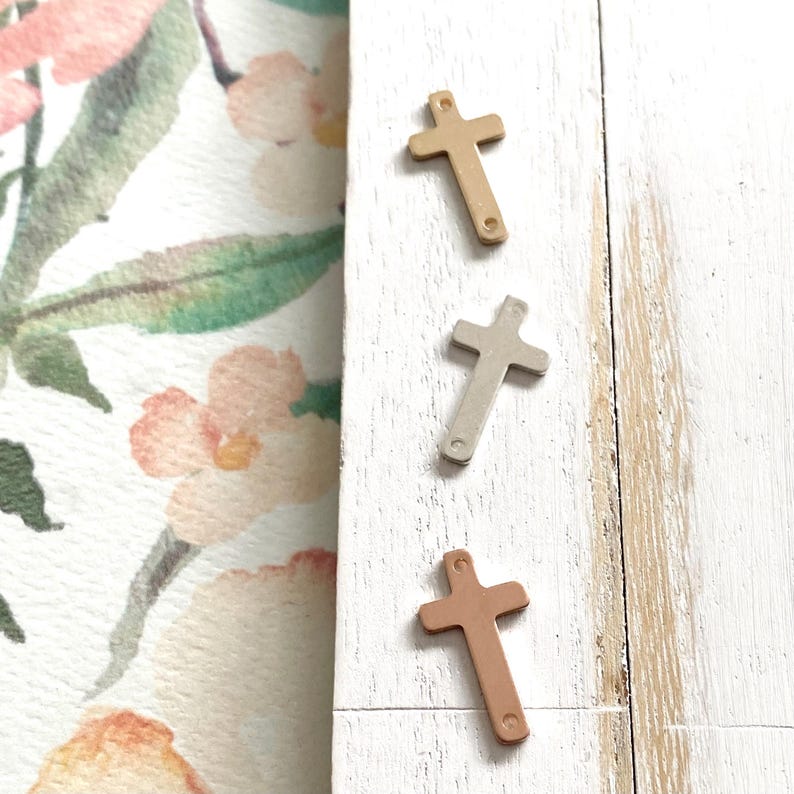 May include: Three metal cross charms in gold, silver, and rose gold.