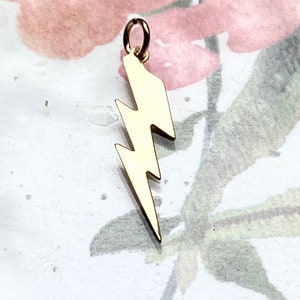 May include: Gold lightning bolt charm pendant. The charm is made of solid gold and has a smooth, polished finish.