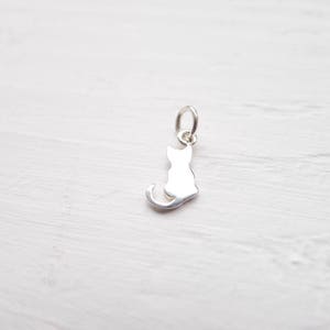 Tiny flat sitting cat charm silhouette.  Very little pendant with tail of the cat to the side.