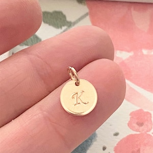 May include: Gold charm with the letter K engraved on a round disc.