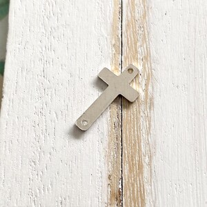 May include: Silver metal cross charm with two holes for attaching to jewelry or other crafts.