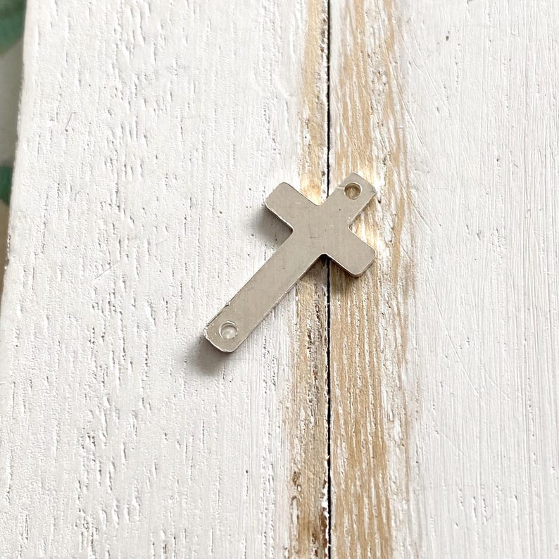 May include: Silver metal cross charm with two holes for attaching to jewelry or other crafts.