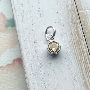 May include: A silver charm with a yellow gemstone. The charm has a loop for attaching to a bracelet or necklace.