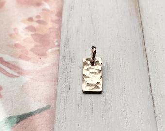 May include: A gold-toned rectangular pendant with a hammered texture and a loop at the top for attaching to a chain.