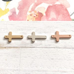 May include: Three metal cross charms in different finishes: gold, silver, and rose gold. The crosses are simple and elegant, perfect for adding a touch of faith to jewelry or crafts.