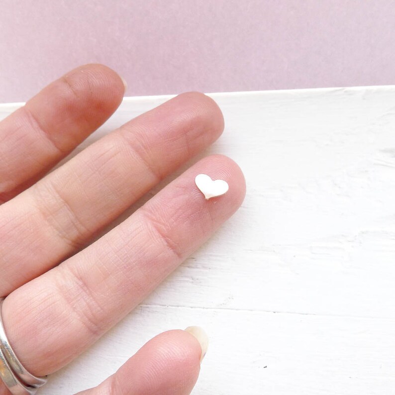 May include: A small white heart-shaped charm on a finger.