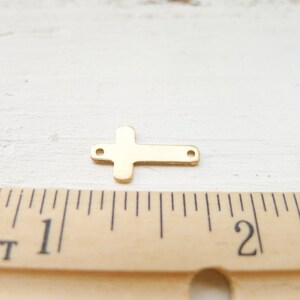 May include: Gold-toned metal cross charm with two holes for attaching to jewelry or other crafts. The cross is about 1 inch long and 1/2 inch wide.