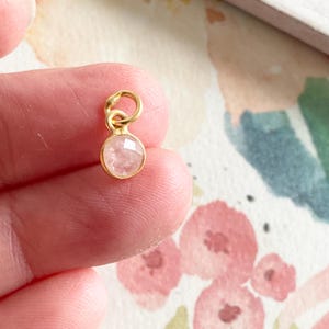 May include: A gold charm with a small, round, clear pink gemstone.