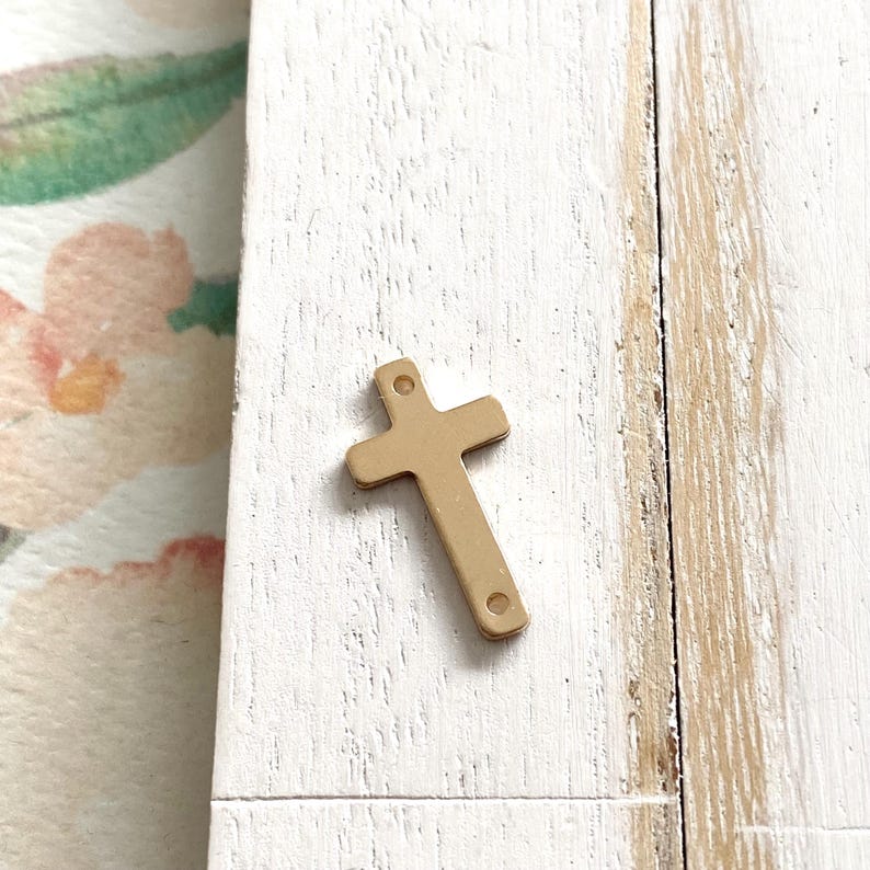 May include: A gold-colored metal cross charm with two holes for attaching to jewelry or other crafts.