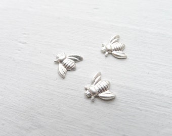 May include: Three silver bee charms on a white background. The bees are detailed and have a realistic appearance.