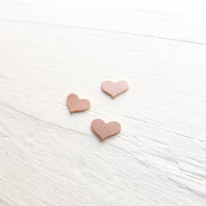 May include: Three small pink heart-shaped decorations on a white wooden surface.