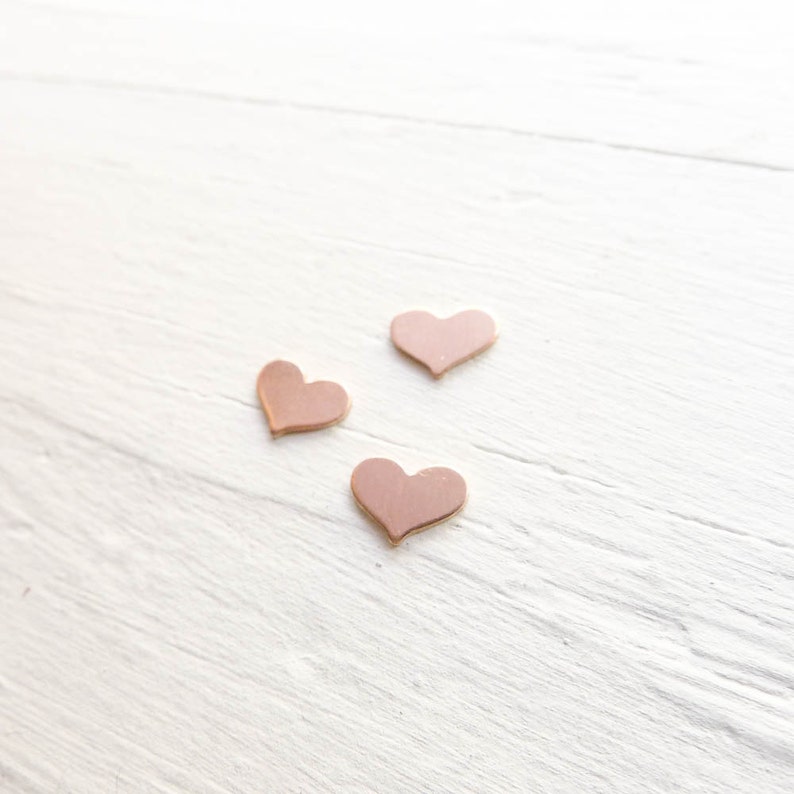 May include: Three small pink heart-shaped decorations on a white wooden surface.
