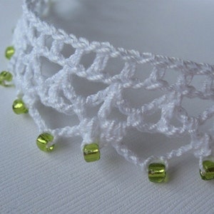 May include: White crocheted lace trim with green glass beads. The trim is delicate and has a scalloped edge.
