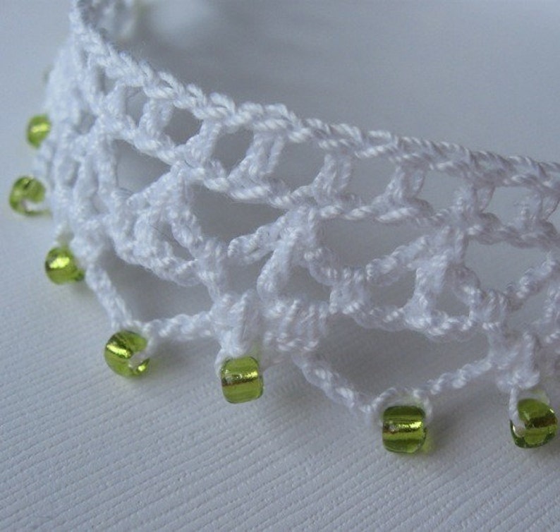May include: White crocheted lace trim with green glass beads. The trim is delicate and has a scalloped edge.
