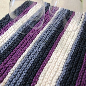 May include: A striped knitted dishcloth in shades of purple, grey, and white. The dishcloth is made with a textured stitch and is perfect for drying dishes or wiping down surfaces.