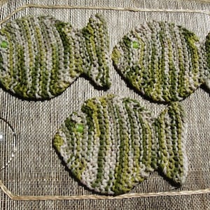 May include: Three knitted fish-shaped dishcloths in green and white. The dishcloths are made with a textured knit pattern.