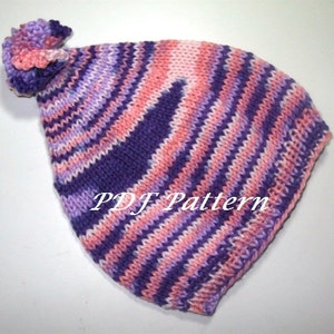 Könnte beinhalten: Eine gestrickte Mütze in Lila und Rosa mit einem passenden Bommel oben. Die Mütze hat ein PDF Pattern-Etikett.