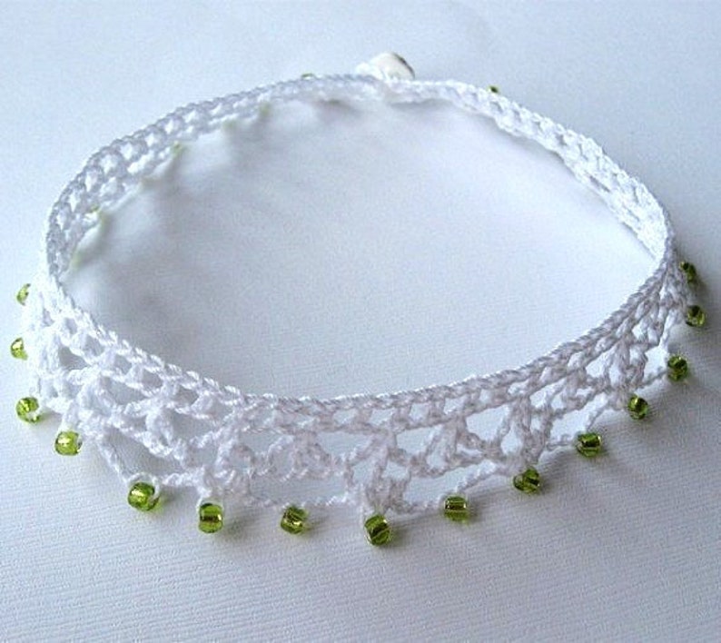May include: White crocheted choker necklace with green beads hanging from the bottom.