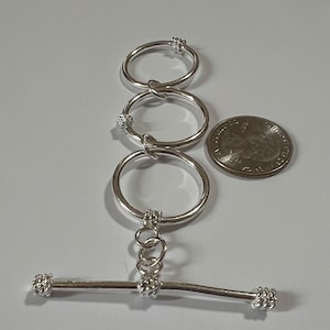 May include: Silver toggle clasp with three interlocking rings. The clasp is approximately the size of a US quarter.