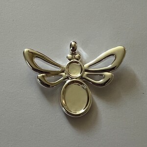 May include: Silver-toned metal pendant shaped like a dragonfly with two oval-shaped areas for adding a cameo or other embellishment.