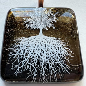 May include: A square glass pendant with a copper bail. The pendant features a white tree with intricate roots on a black background with gold flecks.