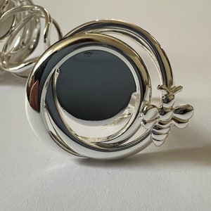 May include: Silver ring with a bee design and a circular design with a black center.
