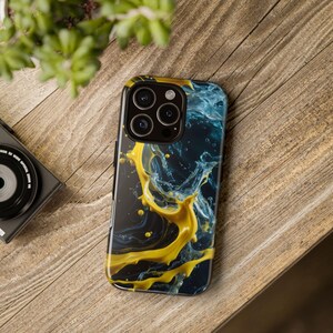 May include: A smartphone case with a vibrant abstract design. The case features a dark background with splashes of yellow and blue, creating a dynamic and artistic look. The case has a black border and a camera cutout.