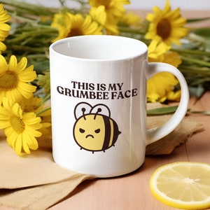 May include: White ceramic mug with a black and yellow cartoon bee illustration and the text "This is my Grumbee Face".