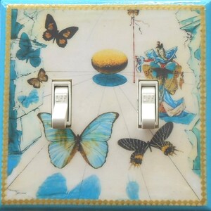 May include: A decorative double light switch cover featuring a butterfly theme. The cover has a light blue border with a gold trim. The design includes butterflies in various colors and sizes, along with an abstract image.