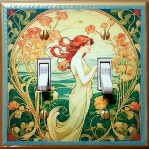 May include: Decorative light switch cover featuring an Art Nouveau design. The cover has a teal border and a gold frame. The artwork depicts a woman with red hair, surrounded by flowers and foliage. The switches are white, and the word "OFF" is printed on them.