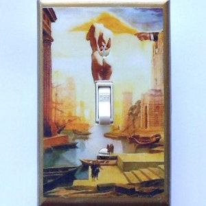 May include: A decorative light switch cover featuring a surrealist painting with a cityscape, boats, and figures. The artwork has warm tones of gold, brown, and orange. The switch is white and in the "off" position. The frame is gold.