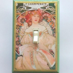 May include: A decorative light switch cover featuring an Art Nouveau style illustration of a woman with floral accents. The artwork is set against a green background with gold trim, and the switch is in the "OFF" position. The text "F. Champenois Paris" is visible.