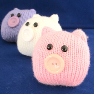 May include: Three knitted pig toys, one purple, one white and one pink. Each pig has black button eyes and a button nose.