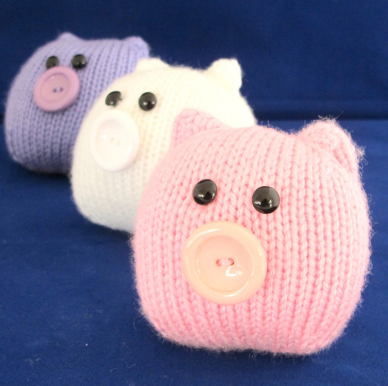 May include: Three knitted pig toys, one purple, one white and one pink. Each pig has black button eyes and a button nose.