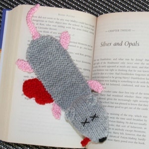 May include: A knitted grey rat bookmark with pink ears and a red heart. The rat has X's for eyes and is lying on a book with the text "Silver and Opals" and "Chapter Twelve".