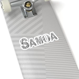 Pode incluir: Um adesivo branco com a palavra "SAMOA" em letras pretas. As letras são preenchidas com um padrão preto e branco.