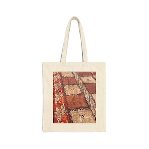 Könnte beinhalten: Cremefarbene Tragetasche mit einem detaillierten Muster in Braun-, Rot- und Beigetönen. Das Design umfasst geometrische Formen und florale Motive. Die Tasche hat ein schlichtes, robustes Design mit langen Henkeln.