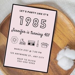 以下が含まれることがあります： ピンクのパーティー招待状に「Let's party like it's 1985 Jennifer is turning 40!」の文字が書かれています。招待状には、日付と時間、住所、RSVP情報が記載されています。招待状は、スクランチー、ローラースケート、ブームボックス、口紅、ファニーパックなど、80年代をテーマにしたアイコンで飾られています。